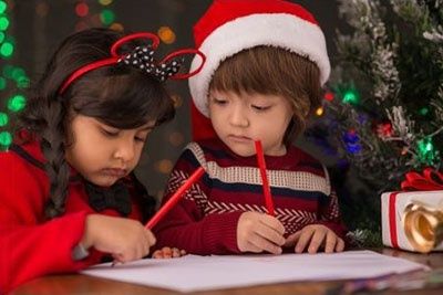 Two children writing a letter beside a decorated Christmas tree
