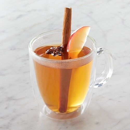 Glass mug of amber spiced cider with cinnamon and apple garnish